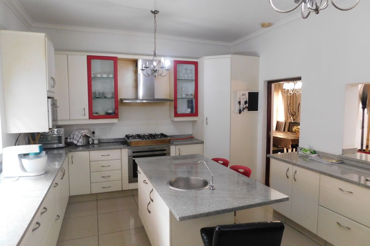 A functional kitchen featuring granite countertops, a central island with a sink, built-in cabinetry, and integrated appliances including a gas hob and oven.