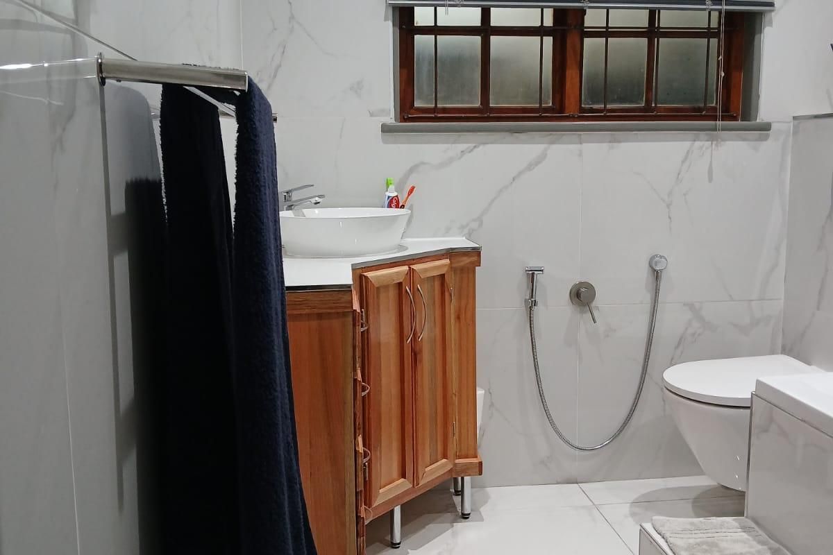 Modern bathroom featuring marble-look wall tiles, a wooden vanity with a vessel sink, wall-mounted toilet, and bidet spray.