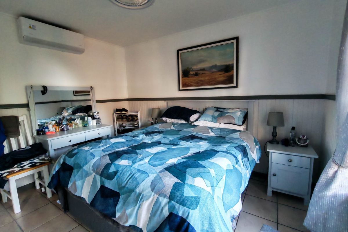A comfortable bedroom featuring tiled flooring, wainscoting wall detailing, and a wall-mounted split-system air conditioner for climate control.