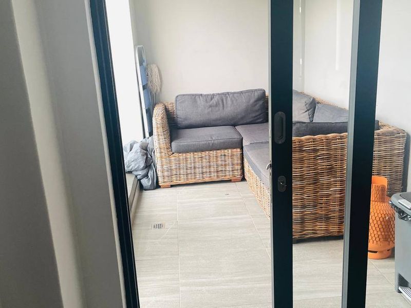 A covered balcony area featuring modern tiled flooring and a sliding glass door entrance, providing a functional outdoor space.