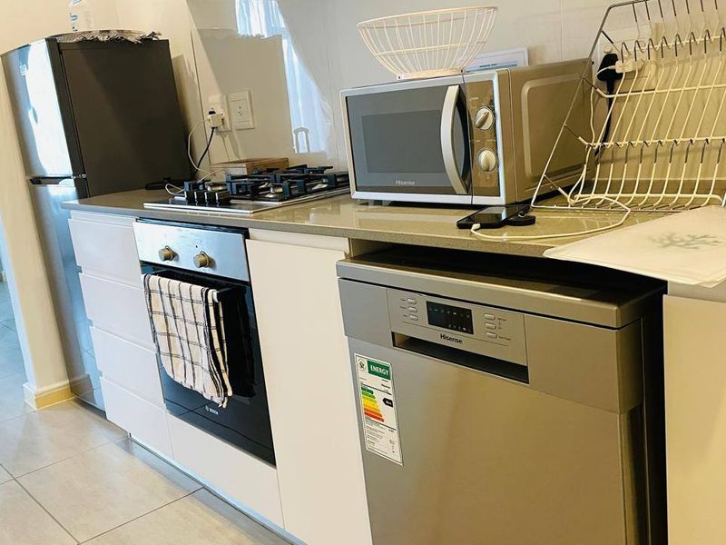 Modern kitchen featuring white cabinetry, stone countertops, a gas hob, built-in oven, and integrated dishwasher, finished with clean tiled flooring.