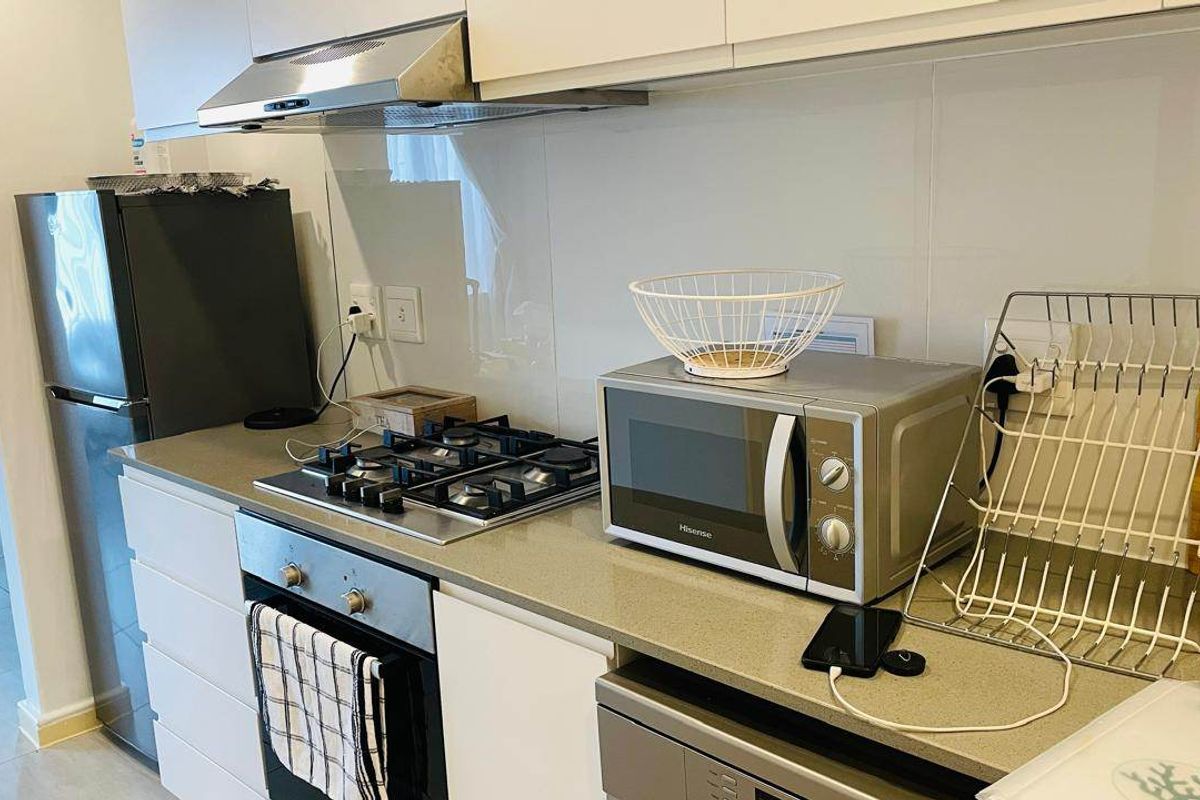 Modern kitchen featuring white cabinetry, stone countertops, a gas hob, built-in oven, and stainless steel extractor fan.