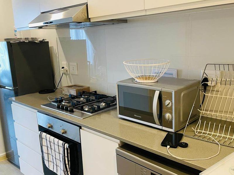 Modern kitchen featuring white cabinetry, stone countertops, a gas hob, built-in oven, and stainless steel extractor fan.
