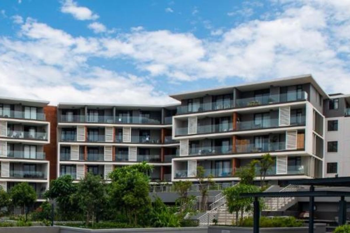 A modern multi-story apartment complex featuring contemporary architecture, glass-fronted balconies, and well-maintained landscaped grounds.