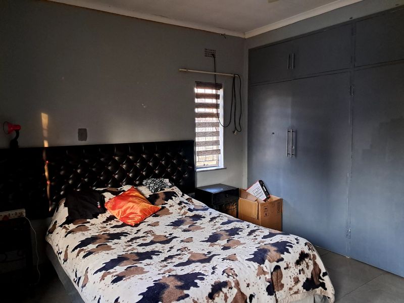 A bedroom featuring built-in cupboards and a window with roller blinds, requiring minor cosmetic updates to improve the overall finish.