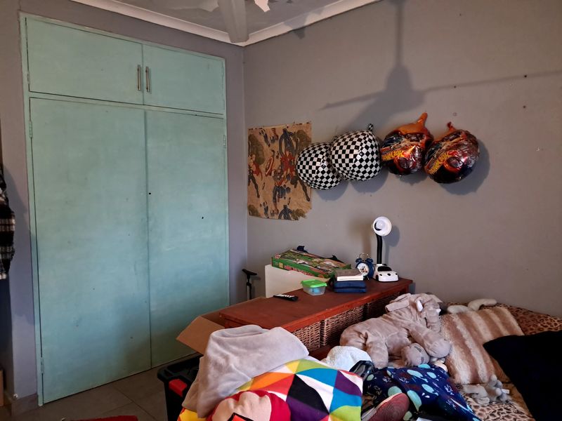 A bedroom featuring a built-in wardrobe and a ceiling fan, currently showing signs of wear on the wall surfaces.