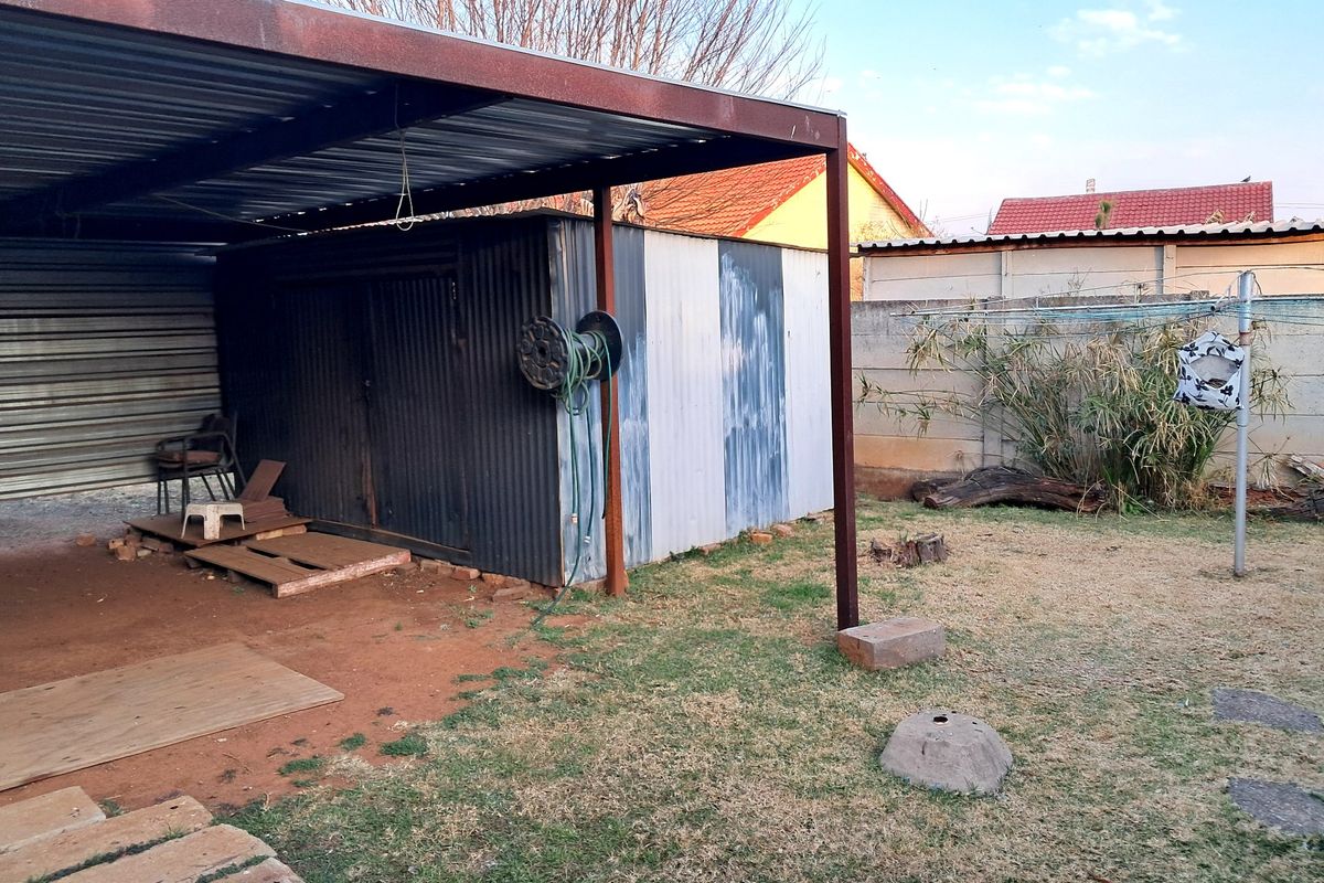Rear yard area featuring a corrugated metal carport and storage shed, enclosed by a precast concrete boundary wall.