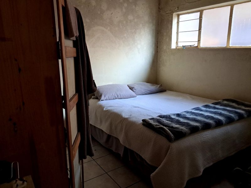 A bedroom featuring tiled flooring and a window with security bars, currently showing significant wear and staining on the wall surfaces.