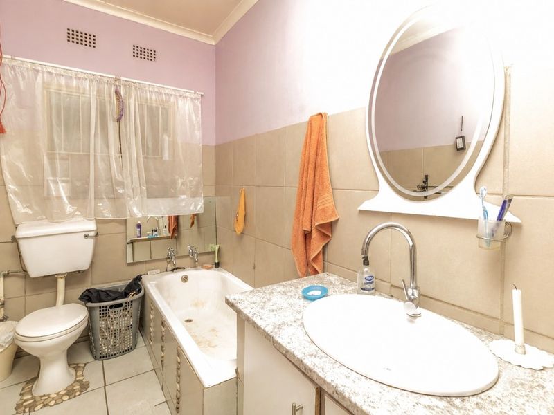 A functional bathroom featuring a bathtub, toilet, and vanity basin with tiled walls and flooring, currently requiring cosmetic updates and maintenance.