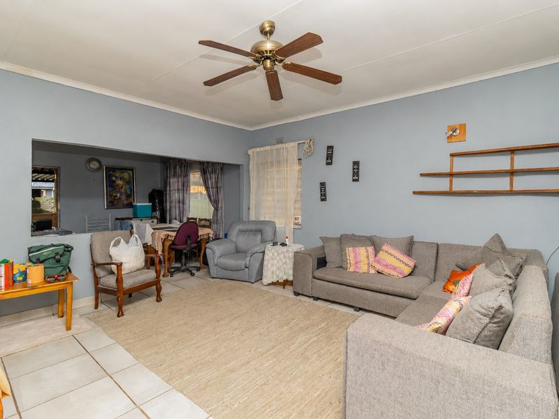 Open plan living area featuring tiled flooring, a ceiling fan, and wall-mounted shelving, offering a versatile space for relaxation and dining.