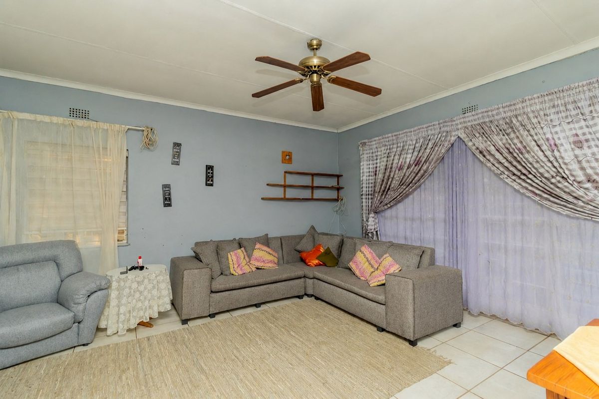 A living room featuring tiled flooring, a ceiling fan, and large windows with curtain rails, offering a functional space ready for cosmetic updates.