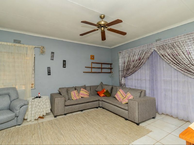 A living room featuring tiled flooring, a ceiling fan, and large windows with curtain rails, offering a functional space ready for cosmetic updates.