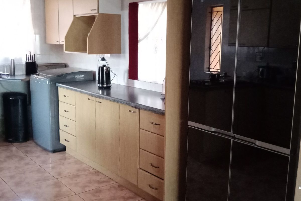 A functional kitchen featuring light wood-tone cabinetry, laminate countertops, and ceramic floor tiles, providing a practical workspace with integrated sink and hob.