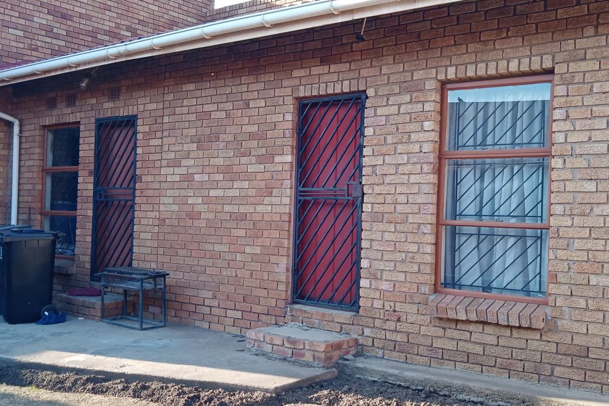 Rear exterior view of a face brick house featuring multiple access points with security gates and window bars.