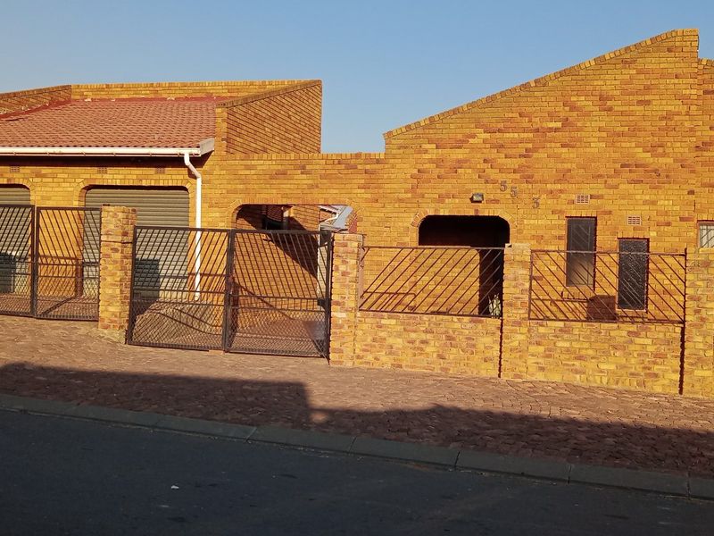 Front elevation of a face brick house featuring a paved driveway, secure metal gates, and integrated garage access.