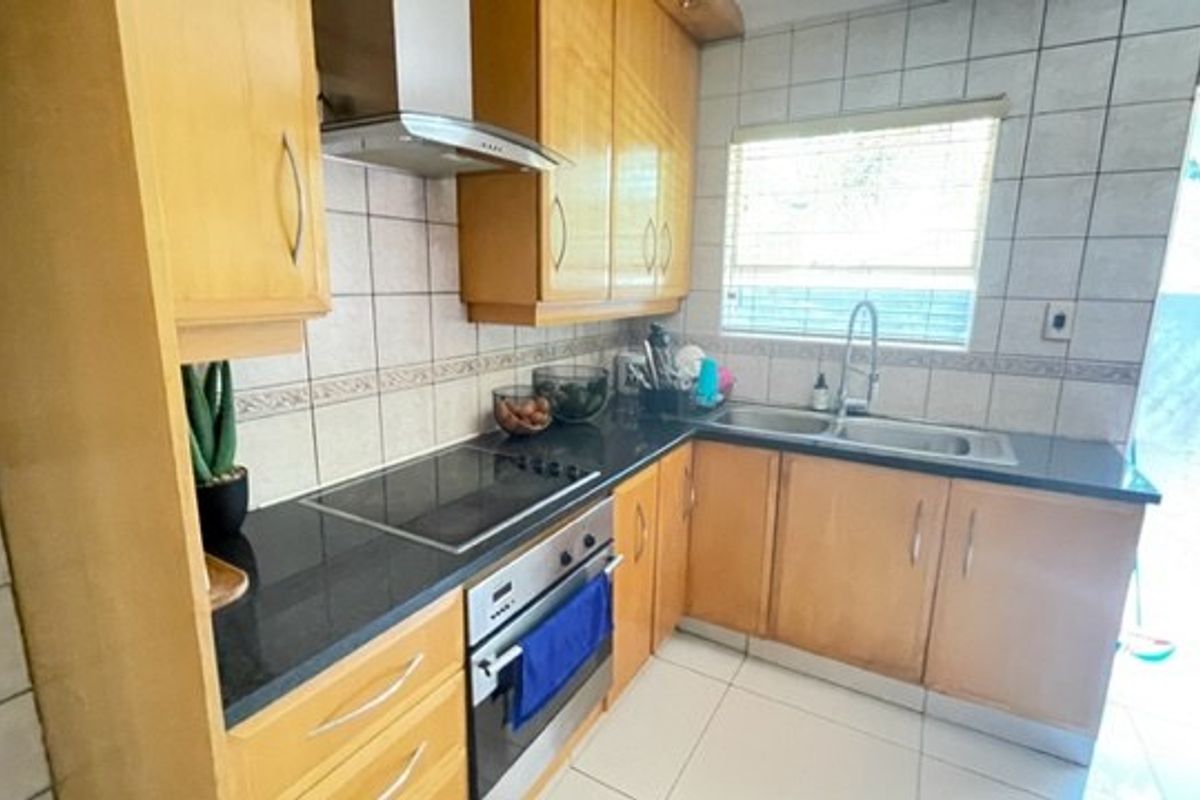 A functional kitchen featuring light wood cabinetry, granite countertops, a built-in oven, electric hob, and tiled splashbacks with direct access to the exterior.