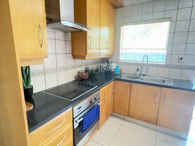 A functional kitchen featuring light wood cabinetry, granite countertops, a built-in oven, electric hob, and tiled splashbacks with direct access to the exterior.