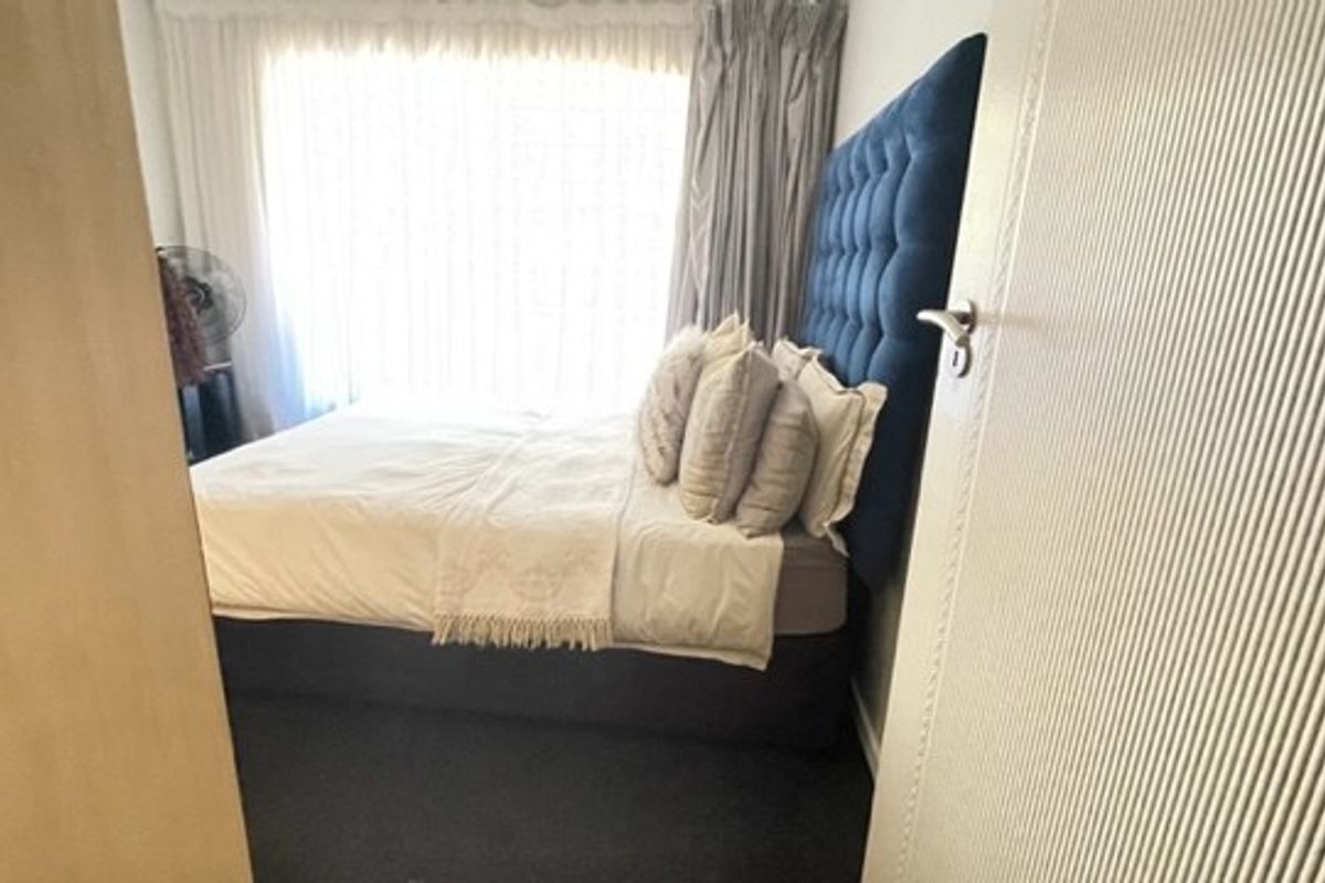 A compact bedroom featuring carpeted flooring and natural light through a window with curtain tracks.