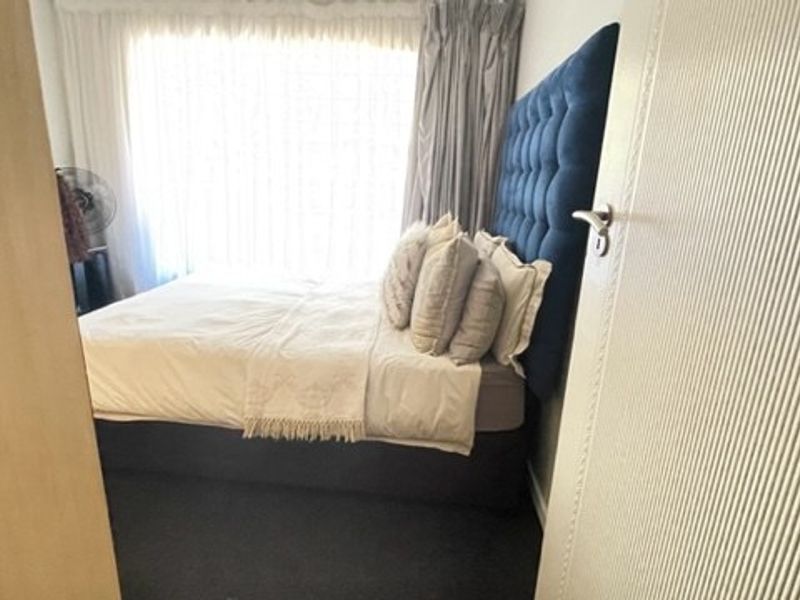A compact bedroom featuring carpeted flooring and natural light through a window with curtain tracks.