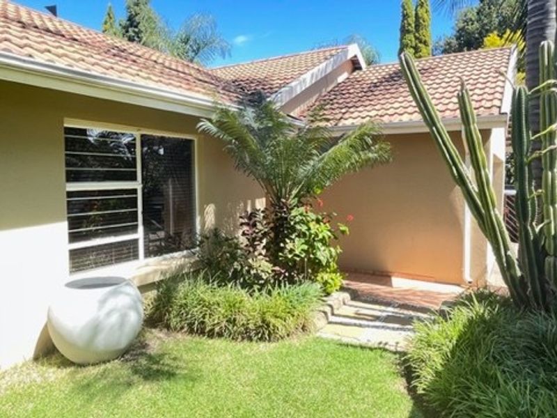 A well-maintained rear exterior view featuring a tiled roof, landscaped garden, and paved walkway leading to the home entrance.