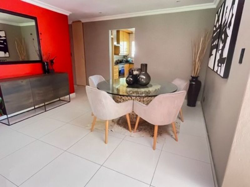 A bright dining room featuring large format floor tiles, recessed lighting, and coved cornicing, with a direct view into the adjacent kitchen area.