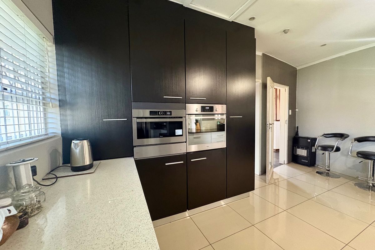 Modern kitchen featuring dark cabinetry, integrated stainless steel appliances, stone countertops, and polished floor tiles.