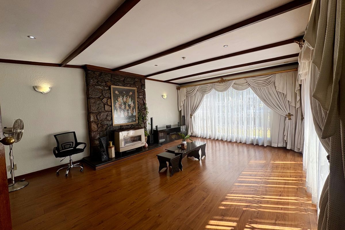 Spacious living room featuring exposed timber ceiling beams, a prominent stone feature wall with a built-in fireplace, and warm laminate flooring.