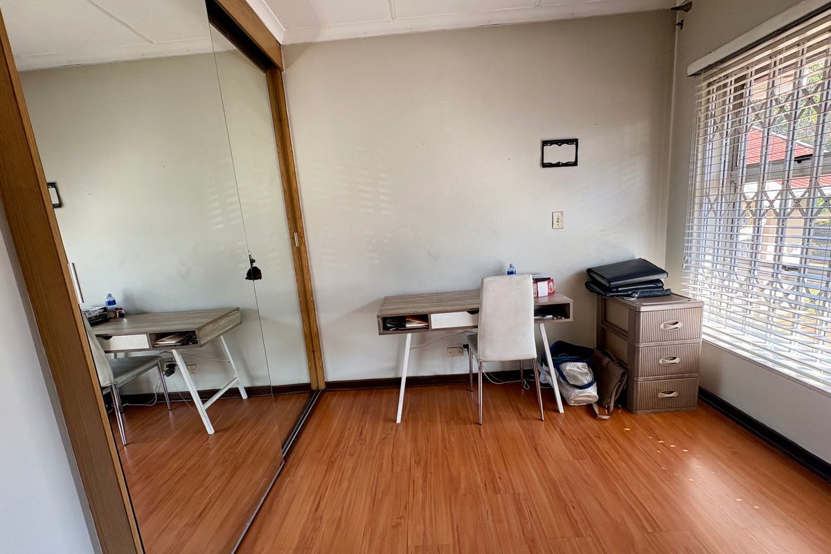 Bedroom featuring laminate flooring, a large mirrored sliding wardrobe, and window with venetian blinds and security bars.