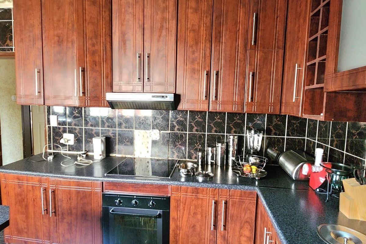 A functional kitchen featuring dark wood-look cabinetry, black tiled backsplash, integrated oven and hob, and dark countertops with a drop-in sink.