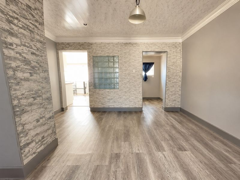 A bright, empty living room featuring modern laminate flooring, stone veneer accent walls, and a decorative glass block insert, offering a clean, neutral canvas.