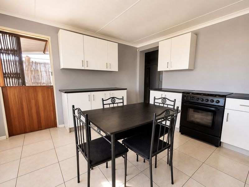 A functional kitchen featuring white cabinetry, dark countertops, a freestanding stove, and tiled flooring, with direct access to an outdoor area via a stable door.
