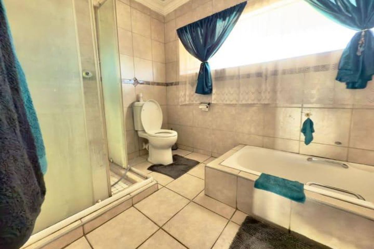 A functional bathroom featuring a built-in bathtub, a separate glass-enclosed shower, and neutral ceramic tiling throughout.