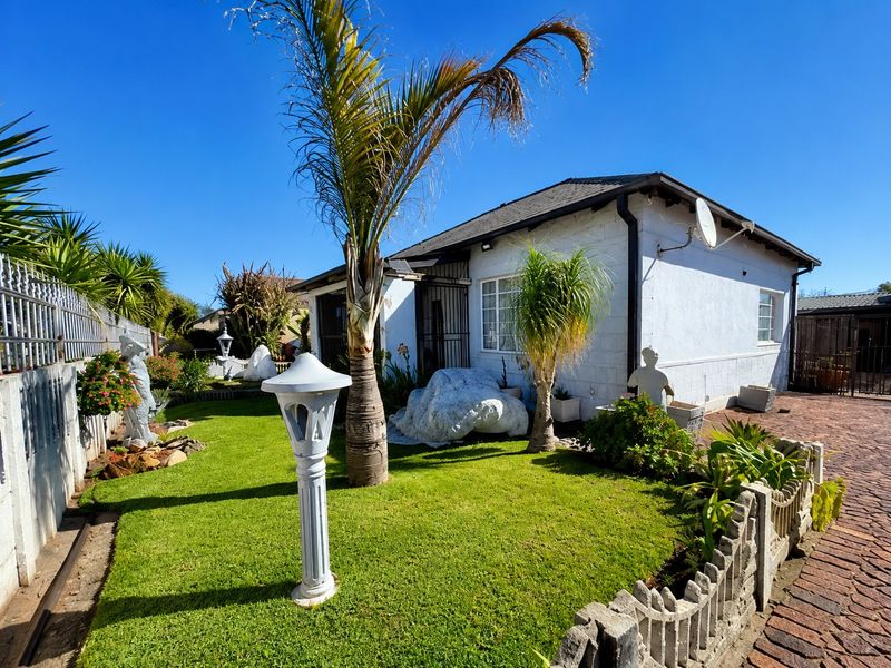 Rear view of the property featuring a landscaped garden, brick paved driveway, and secure boundary walling.