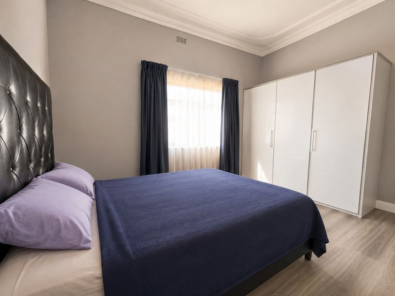 A well-maintained bedroom featuring neutral walls, laminate flooring, decorative cornice, and a large built-in wardrobe.