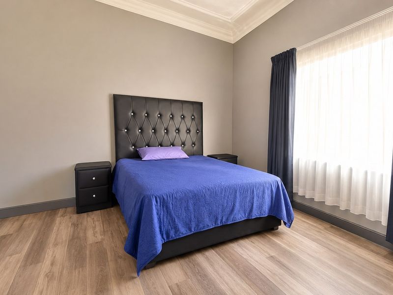 A well-maintained bedroom featuring modern laminate flooring, neutral wall tones, and decorative crown molding, providing a clean and comfortable living space.