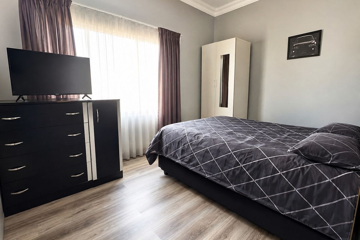 A well-maintained bedroom featuring light-toned laminate flooring, crown molding, and a large window that provides ample natural light.
