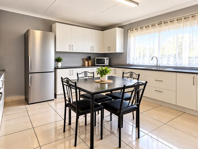 A well-maintained kitchen featuring white cabinetry, dark countertops, stainless steel appliances, and neutral ceramic floor tiles with ample natural light.