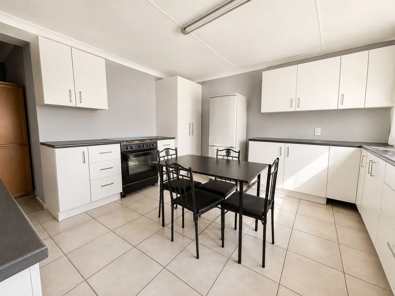 Open-plan kitchen and dining area featuring white cabinetry, dark countertops, built-in oven, and neutral ceramic floor tiles.
