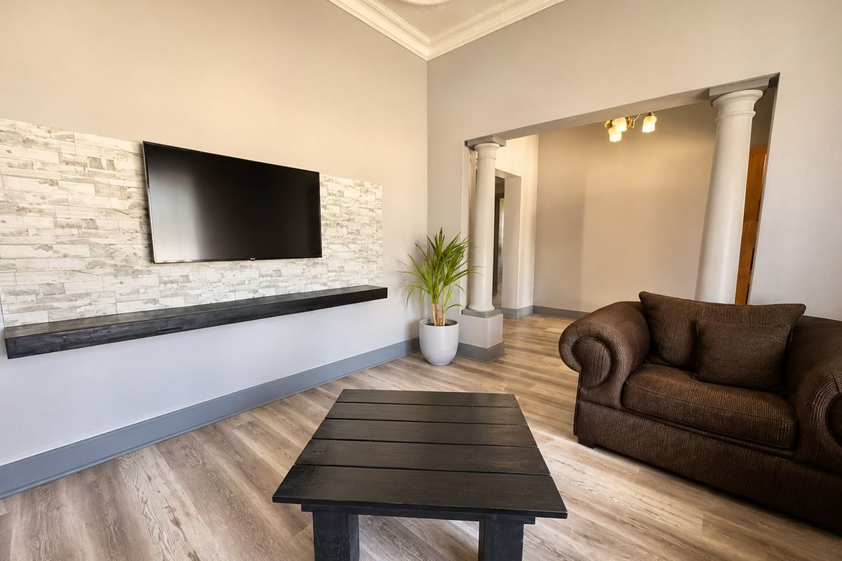 A well-maintained living room featuring a stone-clad feature wall, floating shelf, decorative ceiling details, and architectural columns leading to an adjacent space.