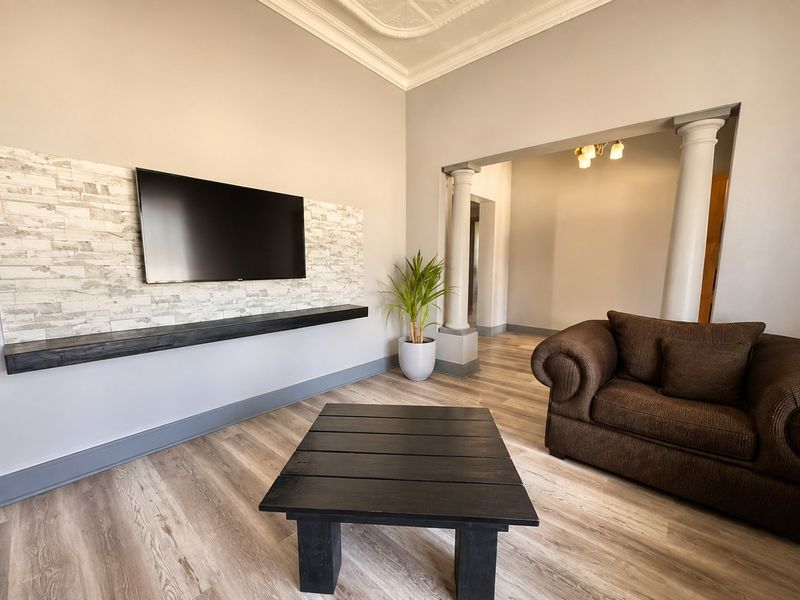 A well-maintained living room featuring a stone-clad feature wall, floating shelf, decorative ceiling details, and architectural columns leading to an adjacent space.
