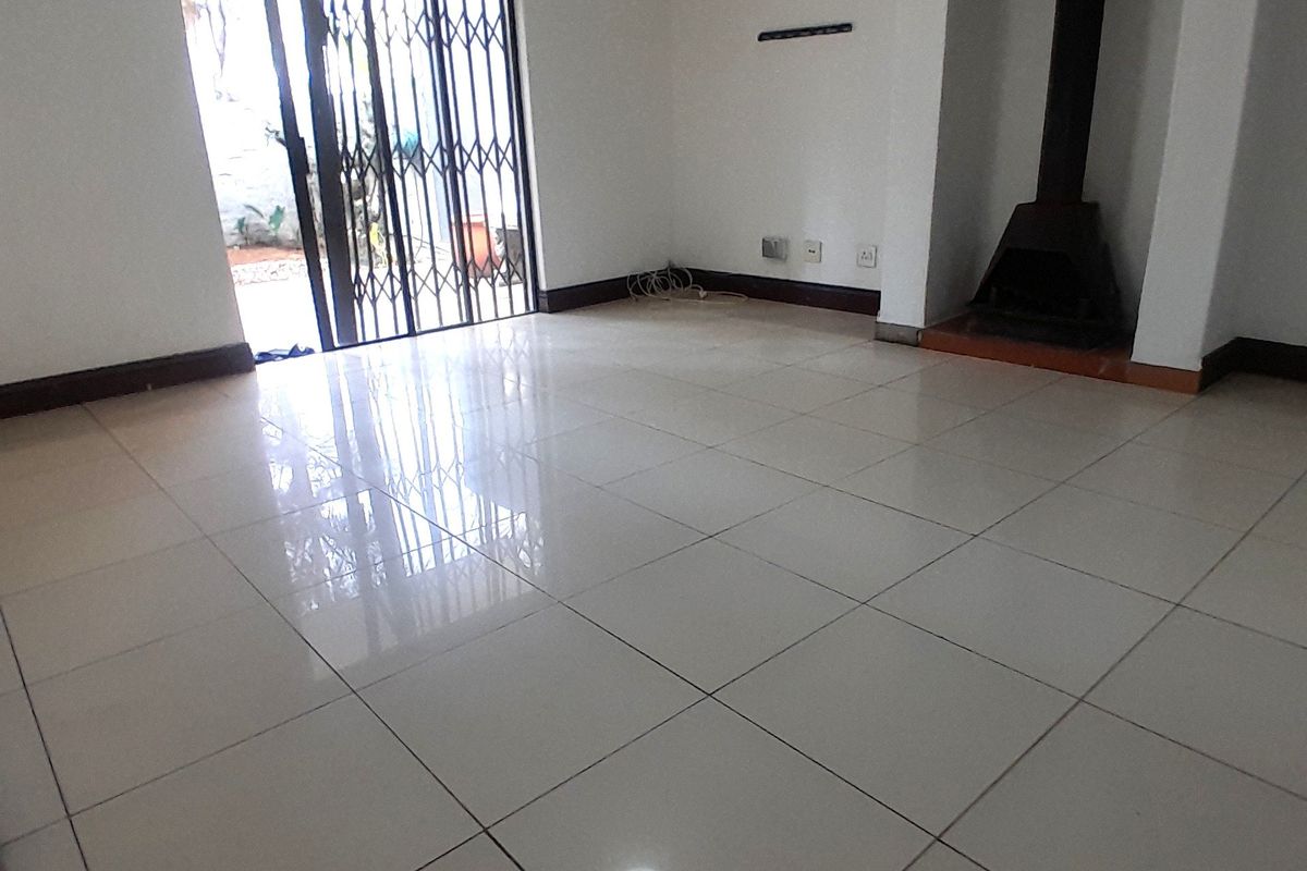 An empty living room featuring polished tile flooring, a built-in fireplace, and a sliding door with a security gate leading to the exterior.