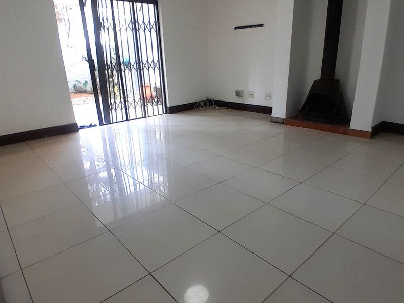 An empty living room featuring polished tile flooring, a built-in fireplace, and a sliding door with a security gate leading to the exterior.
