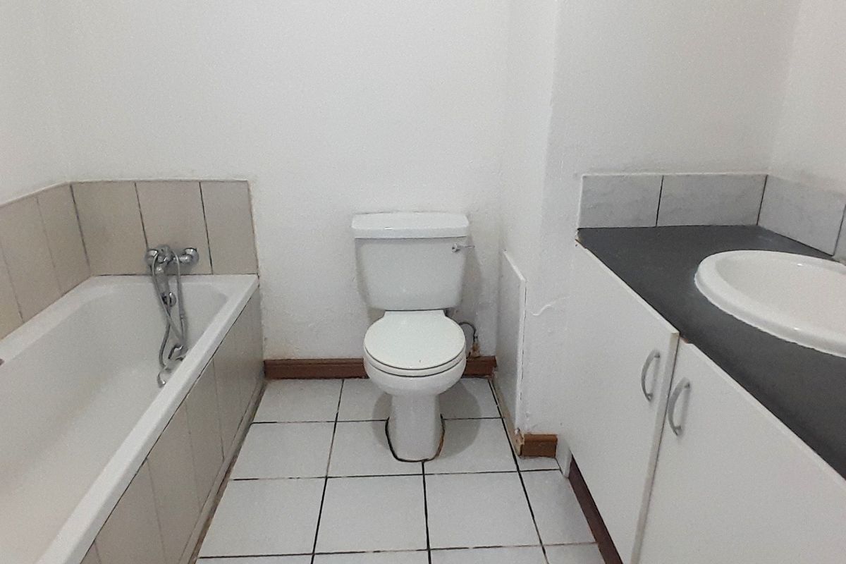 A functional bathroom featuring a bathtub, toilet, and vanity cabinet with a basin, requiring cosmetic updates to the finishes and skirting boards.