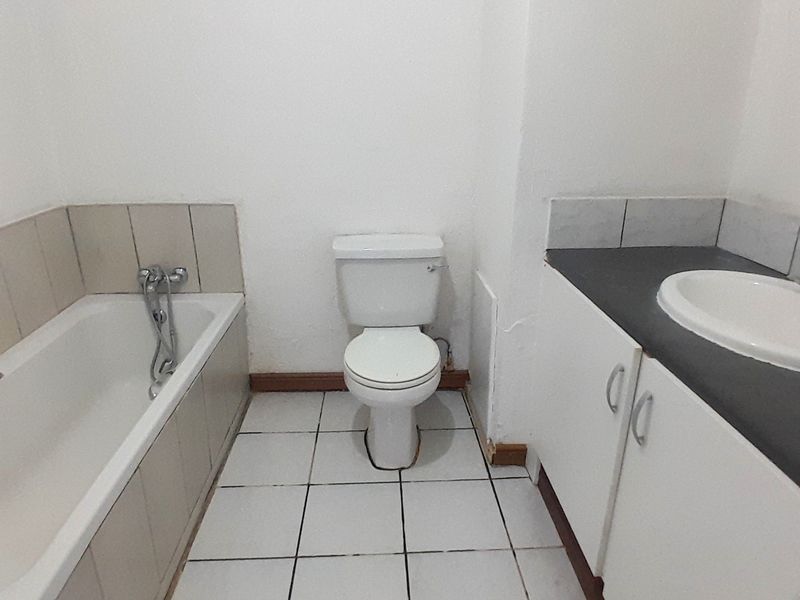 A functional bathroom featuring a bathtub, toilet, and vanity cabinet with a basin, requiring cosmetic updates to the finishes and skirting boards.