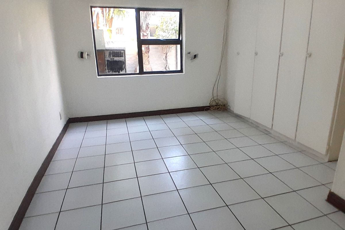 An empty bedroom featuring white tiled flooring, built-in cupboards, and a window with an aluminium frame.
