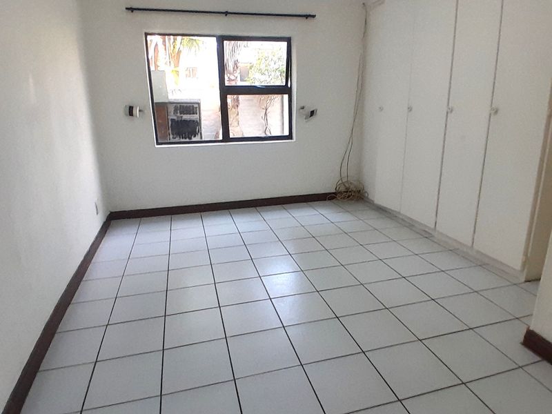 An empty bedroom featuring white tiled flooring, built-in cupboards, and a window with an aluminium frame.