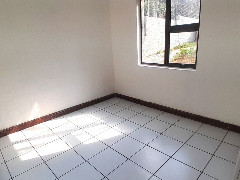 An empty bedroom featuring neutral white walls, tiled flooring, and a large aluminium-framed window providing natural light.