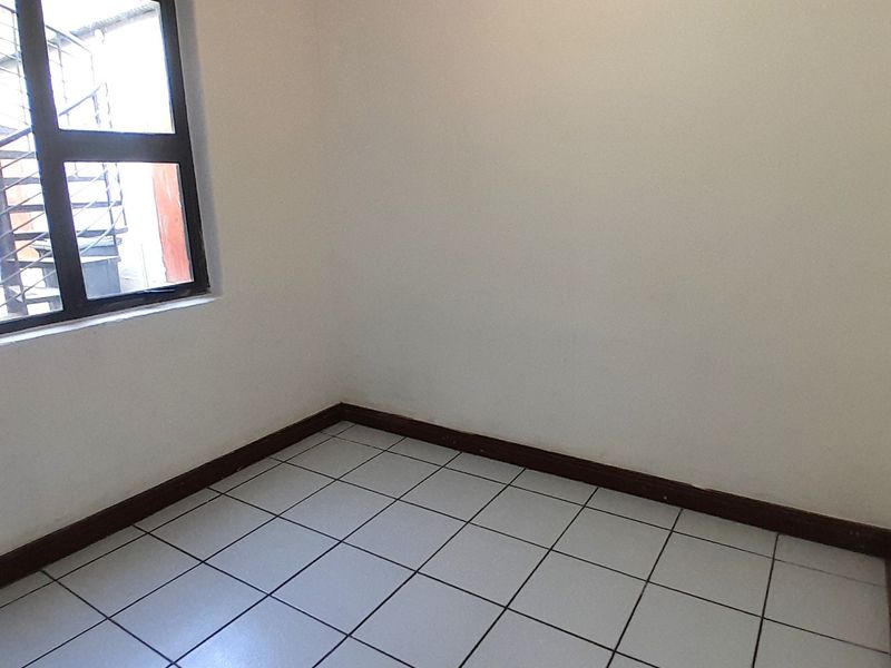 An empty bedroom featuring white walls, tiled flooring, and dark timber skirting boards, providing a blank canvas for interior design.