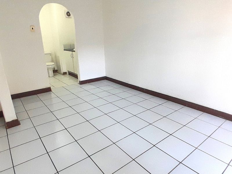 An empty living area featuring white walls, tiled flooring, and a distinctive arched doorway leading to an adjacent space.
