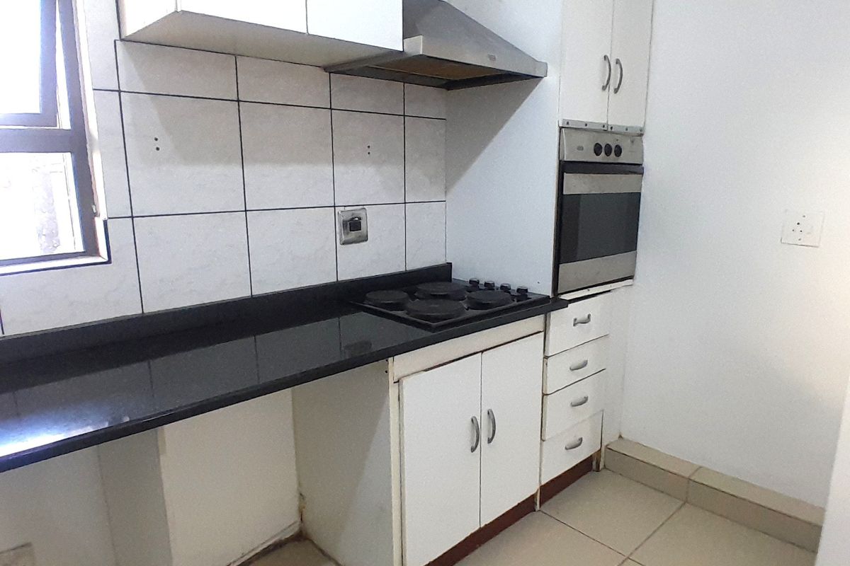 Compact kitchen featuring white cabinetry, black granite countertops, built-in oven, and hob, with tiled flooring and splashback.